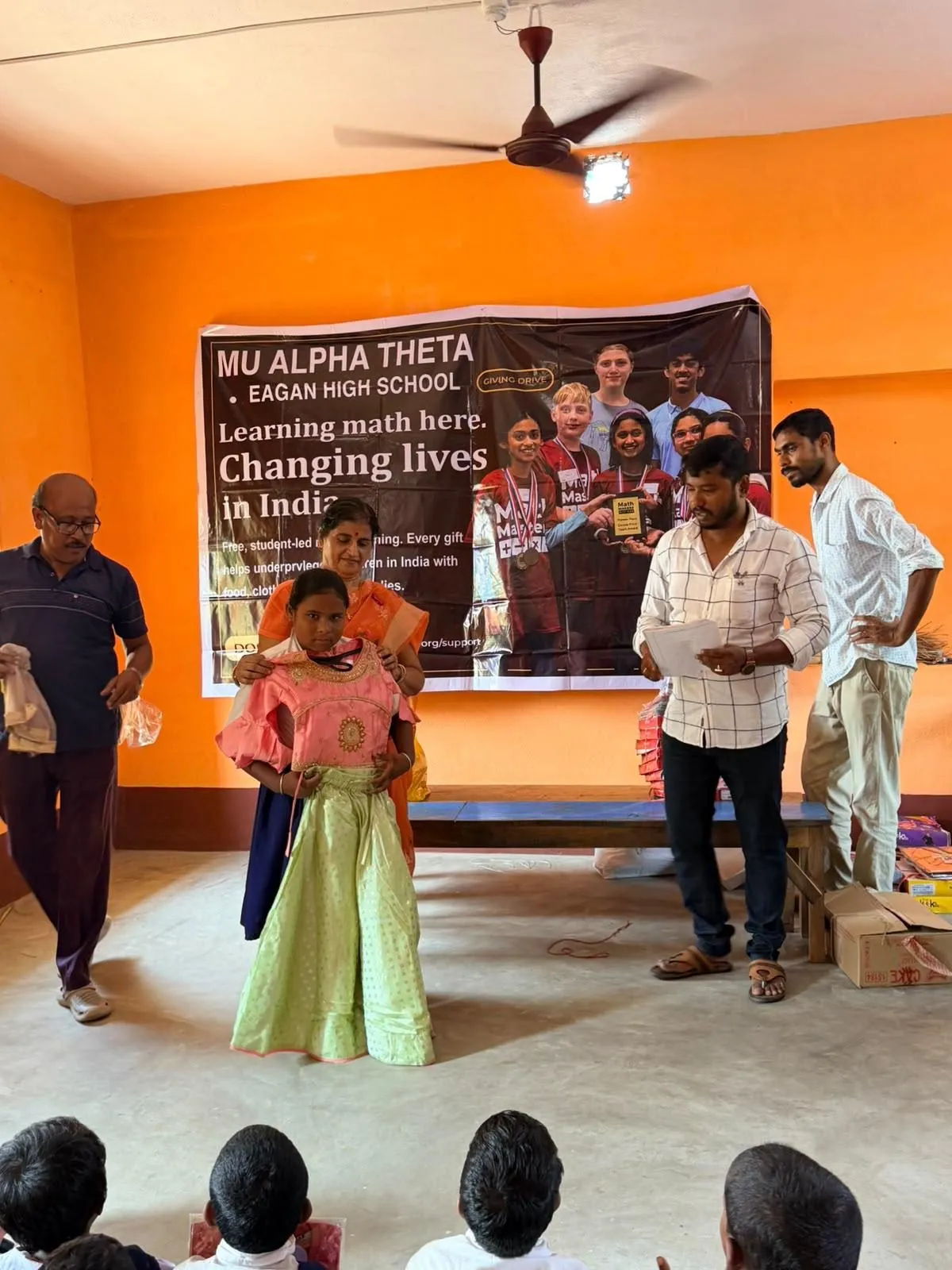 A girl in a new dress stands in front of the banner