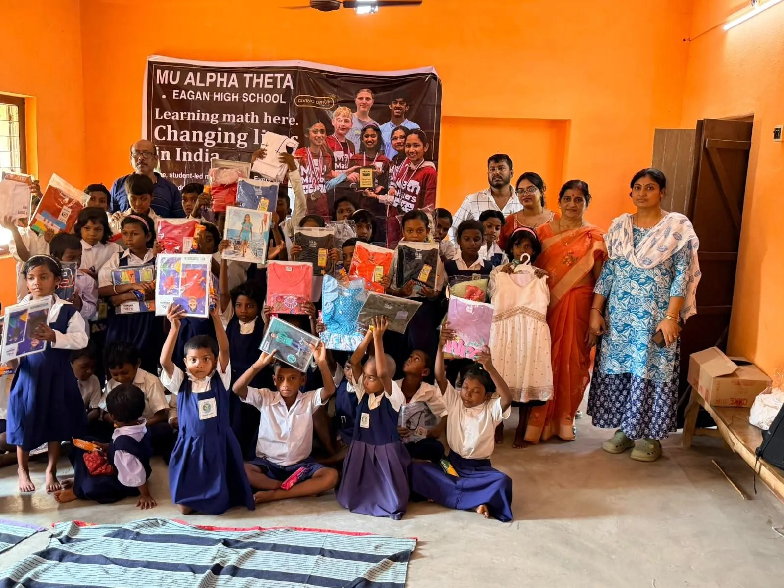 Students hold up new books and school supplies in front of the Mu Alpha Theta banner at the second Giving Drive